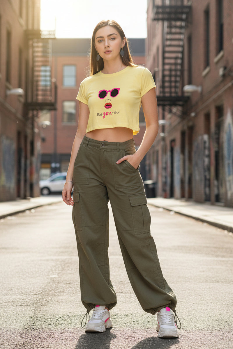 Woman wearing a yellow crop top with sunglasses and lipstick graphic and denim shorts on a white background