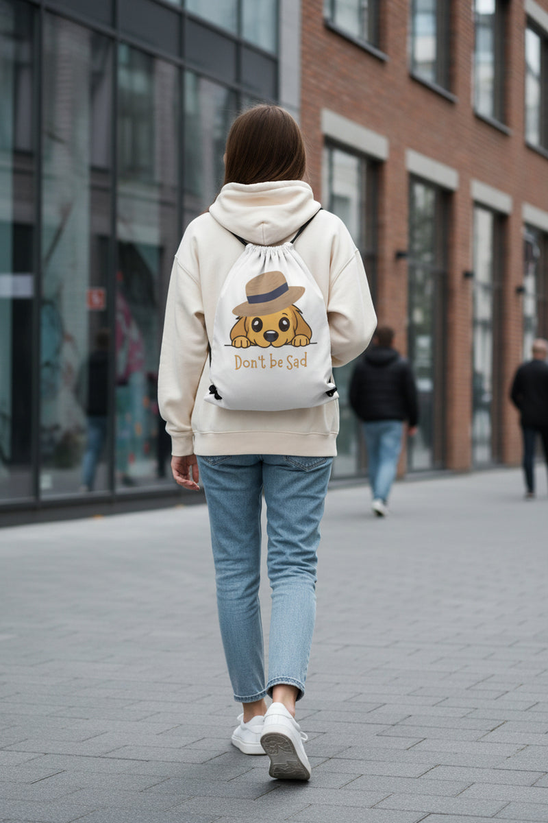 Drawstring bag with a cartoon dog wearing a hat and the text 'Don't be Sad' on a gray background.