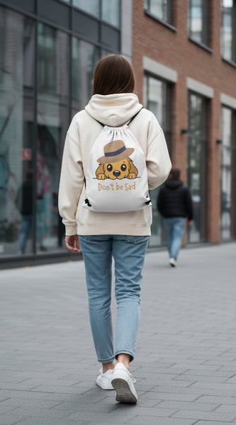 Drawstring bag with a cartoon dog wearing a hat and the text 'Don't be Sad' on a gray background.