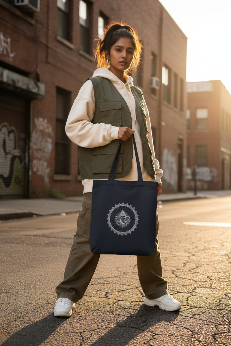 Navy tote bag with a colorful mandala design held by a person against a gray concrete wall.