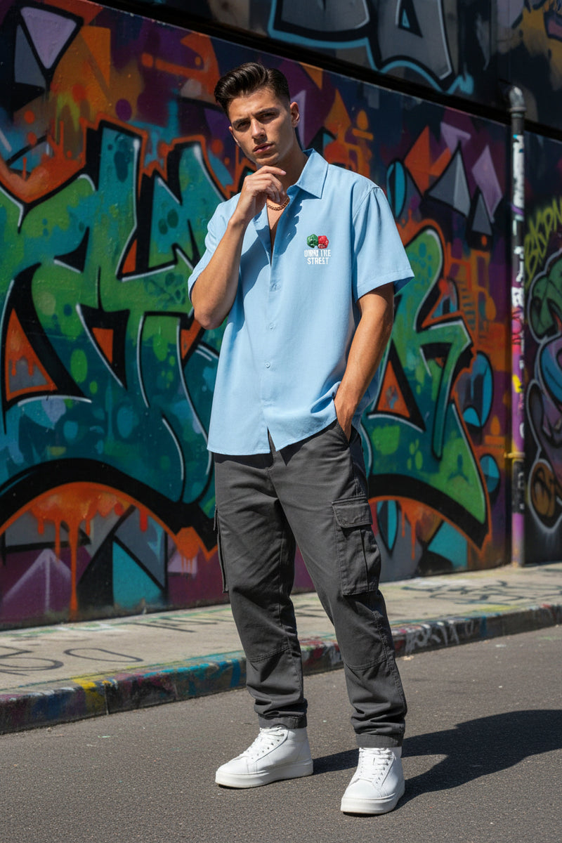 Person wearing a light blue polo shirt with a logo, dark gray cargo pants, and white sneakers standing in front of a colorful graffiti wall.