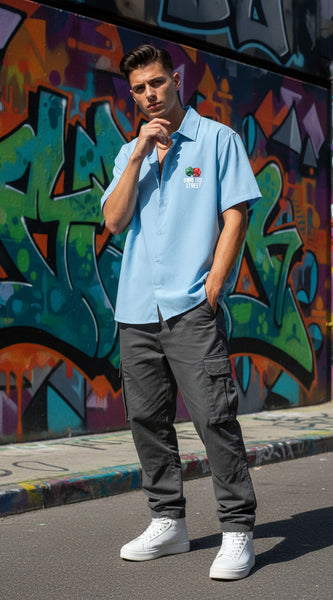 Person wearing a light blue polo shirt with a logo, dark gray cargo pants, and white sneakers standing in front of a colorful graffiti wall.