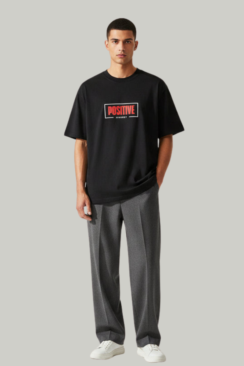 Man wearing a black t-shirt with a red and white logo and gray pants on a light gray background