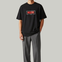 Man wearing a black t-shirt with a red and white logo and gray pants on a light gray background