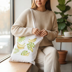 Tote bag with banana and leaf design held by a hand against a white background