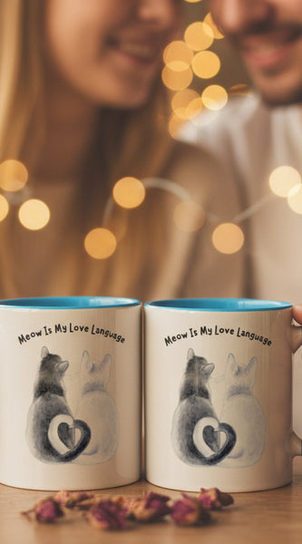 Two mugs with blue handles on a pink background, one featuring a cat illustration and text.